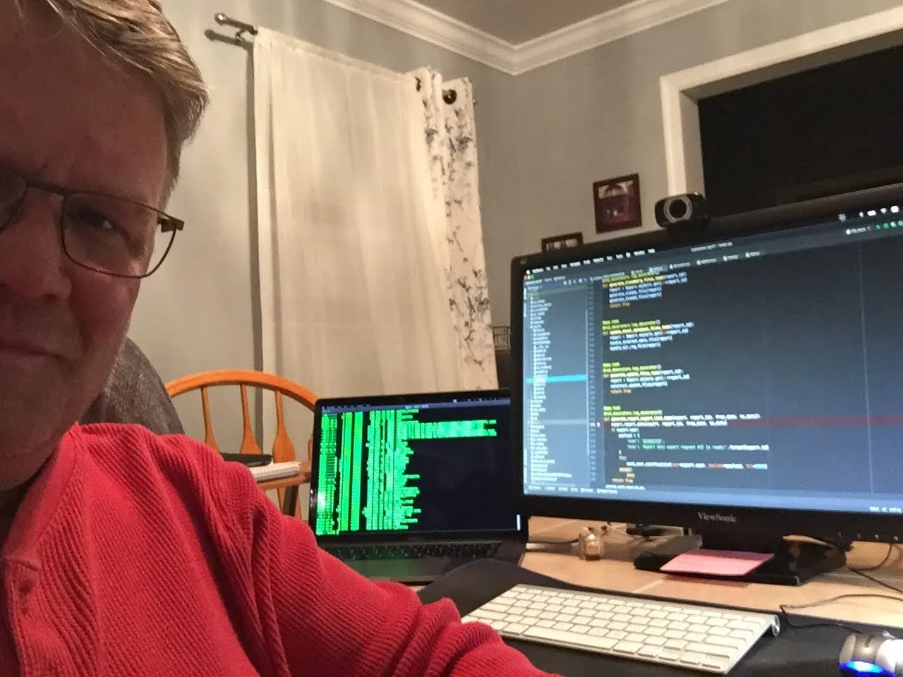 Bill at his desk at night in a red hoodie, a laptop scrolling logs beside a monitor full of code — the Codecenter world headquarters